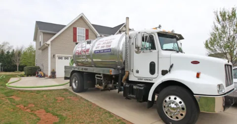 Septic tank pumping truck parked in front of a suburban home